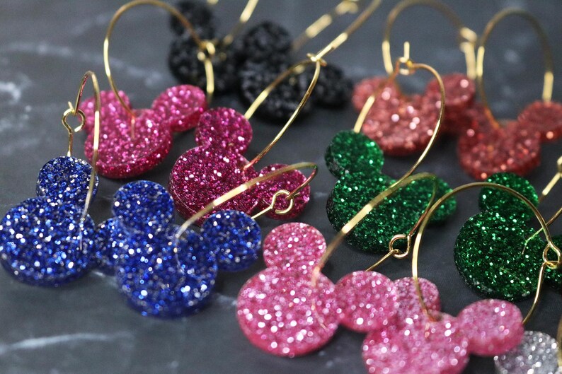 May include: A set of gold hoop earrings with glitter Mickey Mouse head charms in pink, blue, and green.