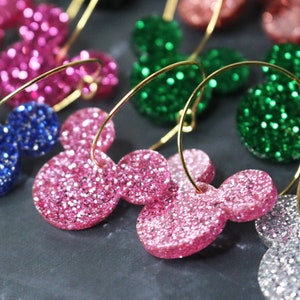 May include: A set of colorful glitter Mickey Mouse earrings with gold hoops. The earrings are pink, green, blue, and silver.