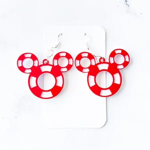 May include: A pair of red and white Mickey Mouse-shaped earrings. The earrings are made of red acrylic and feature a white inner circle and white stripes. The earrings hang from silver-colored fish hook ear wires.