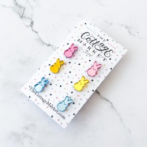 May include: A set of six colorful, reflective, bunny-shaped earrings on a white card with the text "The Cottage Market".