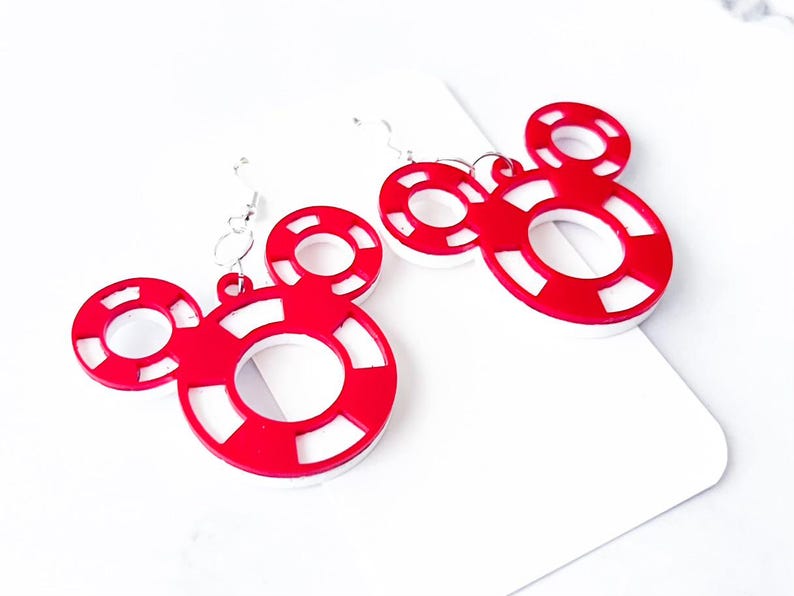 May include: A pair of red and white Mickey Mouse-shaped earrings. The earrings feature a circular design with a white center and red outer ring, connected by silver hooks. The earrings are on a white background.