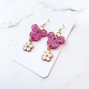 Puede incluir: Pendientes colgantes de Mickey Mouse con purpurina rosa y abalorios de flores blancas.