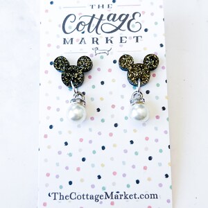 Może przedstawiać: Para złotych kolczyk&oacute;w z motywem Myszki Miki z perłowymi kroplami. Kolczyki są prezentowane na kartce z tekstem "The Cottage Market" i "TheCottageMarket.com".