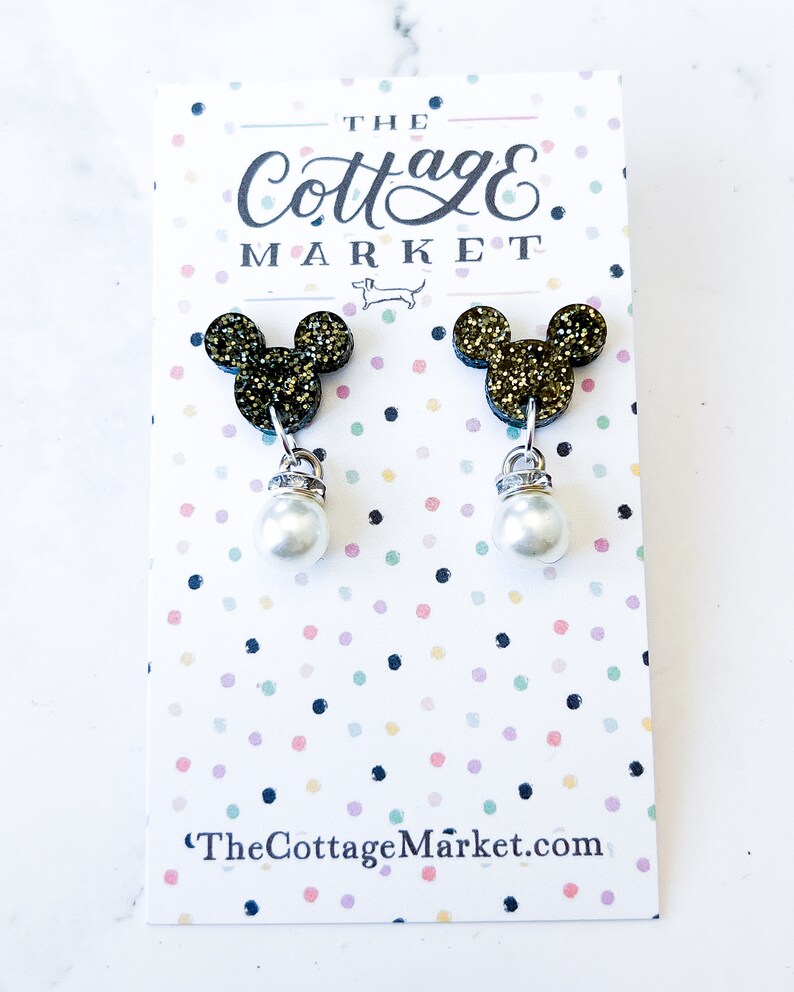 Może przedstawiać: Para złotych kolczyk&oacute;w z motywem Myszki Miki z perłowymi kroplami. Kolczyki są prezentowane na kartce z tekstem "The Cottage Market" i "TheCottageMarket.com".