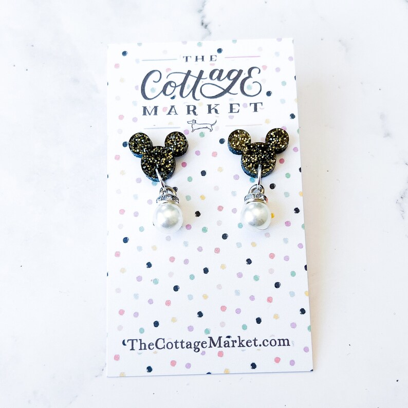 Może przedstawiać: Para złotych kolczyk&oacute;w z motywem Myszki Miki z perłową zawieszką. Kolczyki znajdują się na białej kartce z tekstem "The Cottage Market" i "TheCottageMarket.com".