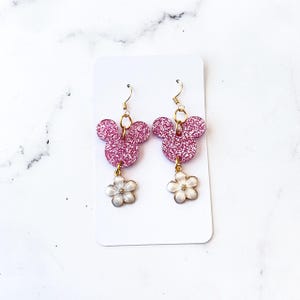 Puede incluir: Pendientes de Mickey Mouse de purpurina rosa con abalorios de flores blancas que cuelgan de ganchos dorados.