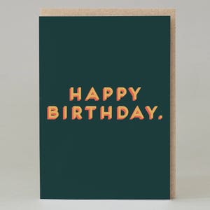 May include: A birthday greeting card with a dark teal background and the words "HAPPY BIRTHDAY." in orange and yellow 3D block letters. The card is set against a light brown background.