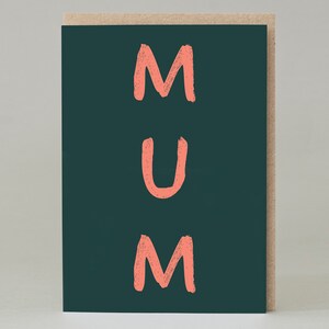 Puede incluir: Una tarjeta de felicitación con la palabra «MUM» en letras de bloque de color coral sobre un fondo verde oscuro. La tarjeta tiene un borde de papel kraft natural.