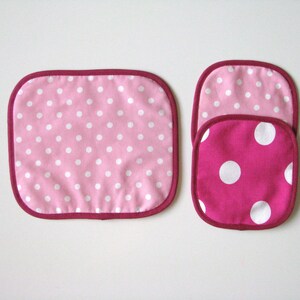 May include: Three pink and white polka dot pot holders. The two smaller pot holders are stacked on top of each other. The larger pot holder is rectangular and the two smaller pot holders are round.