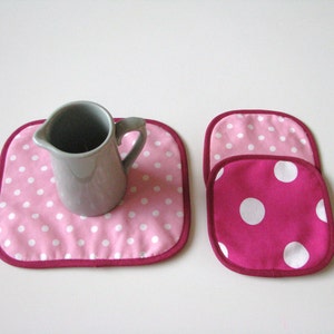 May include: Two pink and white polka dot fabric pot holders with a gray ceramic pitcher on a pink and white polka dot pot holder.