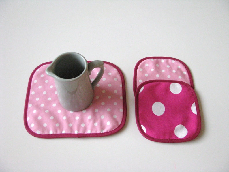 May include: Two pink and white polka dot fabric pot holders with a gray ceramic pitcher on a pink and white polka dot pot holder.