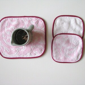 May include: Three pink and white washcloths with burgundy trim. The washcloths are stacked on top of each other.