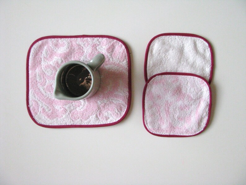May include: Three pink and white washcloths with burgundy trim. The washcloths are stacked on top of each other.
