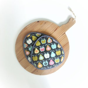 Può includere: Due guanti da forno grigi con un motivo a pere e fiori su un tagliere di legno.