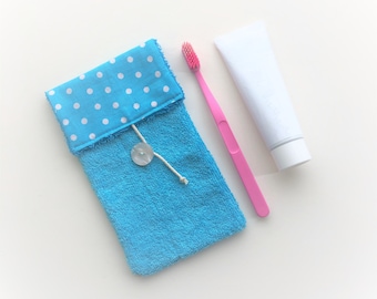 May include: A blue and white polka dot fabric pouch with a blue terrycloth lining and a white button. A pink toothbrush and a white tube of toothpaste are next to the pouch.