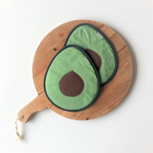 Può includere: Due presine verdi a forma di avocado con centri marroni su un tagliere di legno.