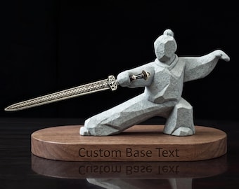 May include: A grey stone-textured figurine of a martial artist in a lunging stance, holding a metallic sword with a detailed pattern. The figure is mounted on an oval wooden base with the engraved text Custom Base Text on the front side.