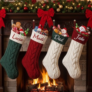 Peut inclure: Quatre bas de Noël en tricot torsadé sont suspendus au-dessus d'une cheminée, chacun avec un nom différent : Lucia, Madi, Dad et Jake. Les bas sont remplis de cadeaux et de jouets. Une guirlande, des nœuds et des bougies décorent la cheminée.