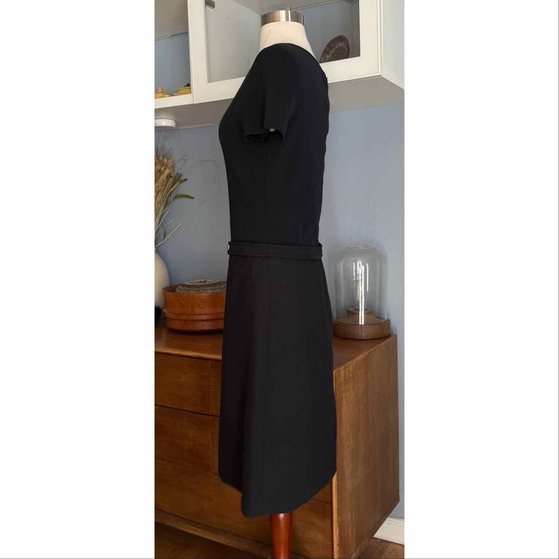 May include: A black dress with short sleeves and a fitted waist. The dress is displayed on a mannequin. The dress has a simple, classic design, suitable for various occasions. The fabric appears to be a smooth, solid material.