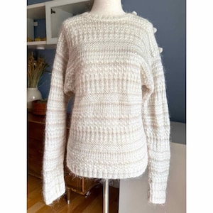 May include: Cream-colored sweater with a round neckline and long sleeves. The knitwear features horizontal stripes of light brown and a textured pattern. The sweater is displayed on a mannequin.