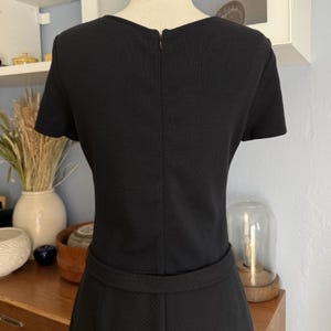 May include: A black dress with short sleeves and a textured pattern. The dress features a fitted waist and a zipper closure at the back. The dress is displayed on a mannequin.