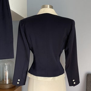 K&ouml;nnte beinhalten: Ein marineblauer Blazer mit wei&szlig;em Kragen und Manschetten. Der Blazer hat eine figurbetonte Silhouette und ist aus glattem Stoff gefertigt.