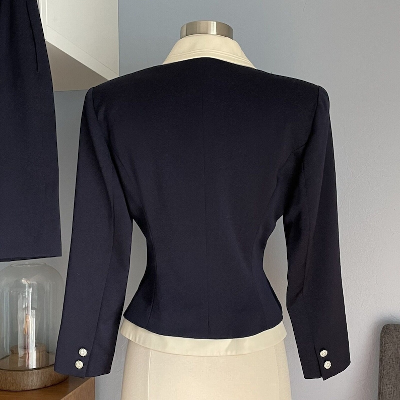 K&ouml;nnte beinhalten: Ein marineblauer Blazer mit wei&szlig;em Kragen und Manschetten. Der Blazer hat eine figurbetonte Silhouette und ist aus glattem Stoff gefertigt.