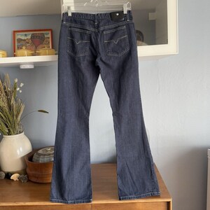 May include: A pair of dark blue denim jeans with a subtle striped pattern. The jeans have a bootcut style and a diamond-shaped logo on the back waistband.