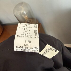 May include: Close-up of a black garment tag with Japanese text and fabric composition percentages. The tag reads "11AR TAKH MADE IN JAPAN". A small white tag with the brand name "sabe" is also visible.