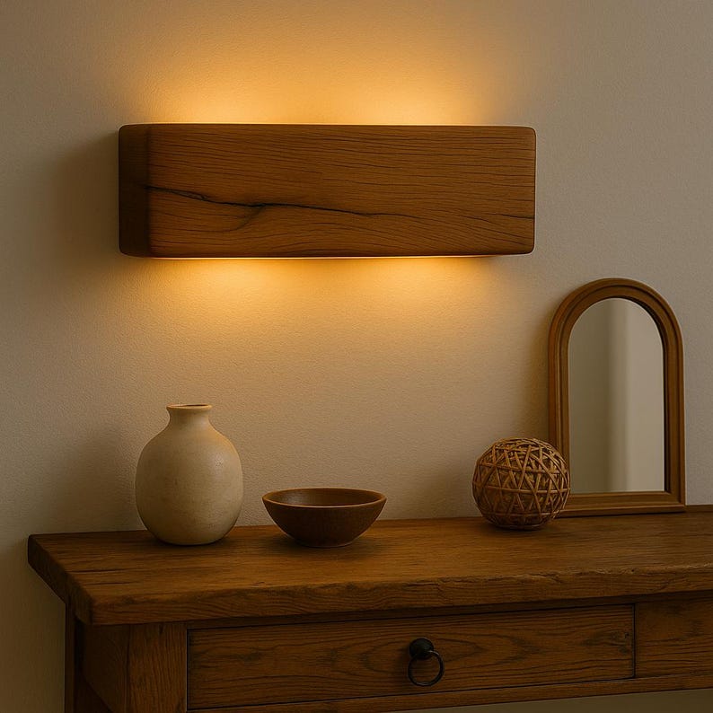 Peut inclure: Un appliques mural rectangulaire en bois avec un &eacute;clairage chaleureux illumine une console en bois. La table pr&eacute;sente un vase, un bol, une sph&egrave;re d&eacute;corative et un miroir en arc encadr&eacute;. L'applique mesure environ 61 cm de long.