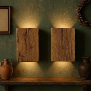 Peut inclure: Deux appliques murales rectangulaires en bois avec une lumière chaude dirigée vers le bas. Les appliques sont en bois texturé brun clair, montées sur un mur vert foncé. Une étagère en bois et des objets décoratifs sont visibles en dessous.