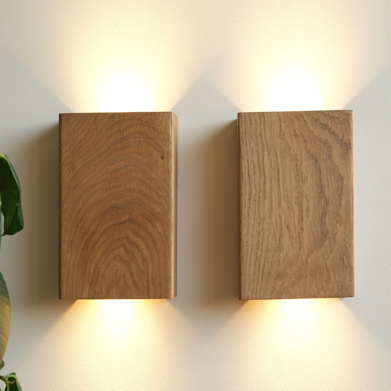 Op de afbeelding: Twee rechthoekige houten wandlampen met ge&iuml;ntegreerde LED-verlichting. De lampen zijn gemaakt van natuurlijk hout met een lichtbruine afwerking. De lampen zijn aan en geven een warm licht.