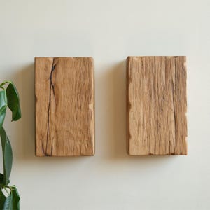 May include: Two rustic wooden wall shelves made from reclaimed wood. The shelves are rectangular and have a natural wood finish. They are mounted on a white wall.
