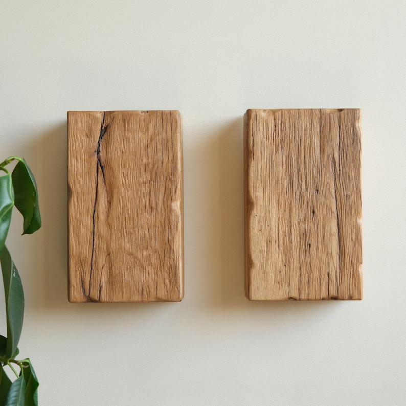 May include: Two rustic wooden wall shelves made from reclaimed wood. The shelves are rectangular and have a natural wood finish. They are mounted on a white wall.