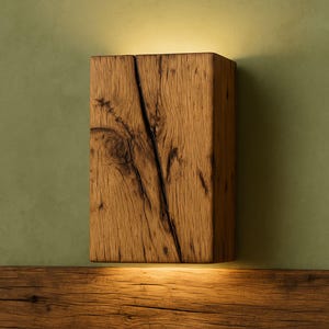 May include: A rectangular, wooden wall sconce with a natural, weathered appearance. The sconce is made from a single block of wood, featuring visible grain and a prominent crack. The warm, brown tones of the wood contrast with the green wall. The sconce is illuminated from below.