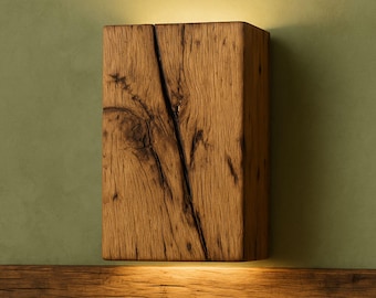 May include: A rectangular, wooden wall sconce with a natural, weathered appearance. The sconce is made from a single block of wood, featuring visible grain and a prominent crack. The warm, brown tones of the wood contrast with the green wall. The sconce is illuminated from below.
