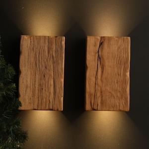 May include: Two rustic wooden wall sconces with warm light emanating from behind them. The sconces are made of reclaimed wood with a natural finish.