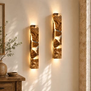 May include: Two rectangular wall sconces featuring a combination of natural brown wood and translucent white resin. The fixtures emit a warm, vertical glow through irregular cracks in the wood, creating a linear light effect on the wall surface.