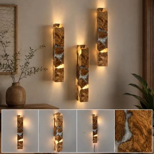 Pode incluir: Três arandelas retangulares feitas de madeira natural e resina branca translúcida. Cada luminária possui orientação vertical com iluminação quente integrada que ilumina os veios da madeira e as seções de resina internamente.