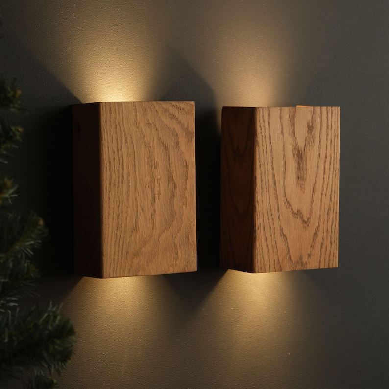 Op de afbeelding: Twee houten wandlampen met warm wit licht dat van de bovenkant van elke lamp schijnt.