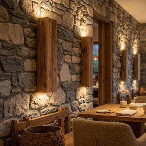 Puede incluir: Interior de un restaurante con paredes de piedra y detalles en madera. Lámparas rectangulares de madera montadas en las paredes. Mesas con cubiertos. El ambiente general es cálido y acogedor.