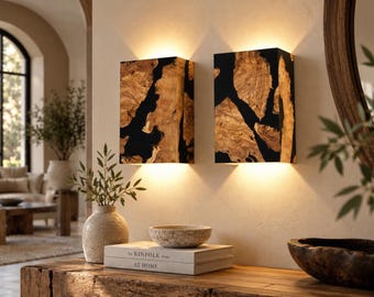 May include: Two rectangular wall sconces featuring a combination of natural light-toned wood grain and solid black resin inserts. Each light fixture is mounted to the wall and emits a warm, soft glow from both the top and bottom edges of the unit.