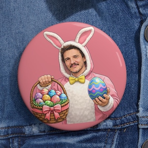 May include: A round, pink button with a cartoon illustration of a person in a pink bunny costume holding a basket of Easter eggs and a decorated egg. The person is wearing a yellow bow tie.