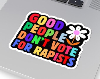 Pode incluir: Um autocolante colorido com o texto "GOOD PEOPLE DON'T VOTE FOR RAPISTS" num arco-íris de cores. Uma margarida branca com centro rosa e caule laranja está ao lado do texto. O autocolante está num computador portátil.
