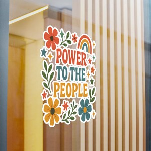 K&ouml;nnte beinhalten: Ein farbenfroher Aufkleber mit dem Schriftzug "POWER TO THE PEOPLE" in einem Retro-Schriftstil. Das Design umfasst Blumen, Sterne, einen Regenbogen und gr&uuml;ne Bl&auml;tter. Der Aufkleber ist eine lebendige Mischung aus Orange, Rot, Blau und Gr&uuml;n.