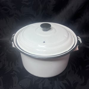 May include: White enamel pot with a lid and black trim. The pot has two handles and a black knob on the lid. The pot is round and appears to be a cooking pot.