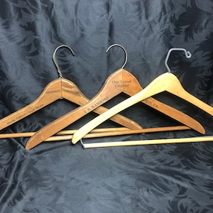 May include: Three vintage wooden hangers with metal hooks. The hangers are labeled "Howard", "J.S. Bashore", and "One Priced Clothier,  Anon, PA".
