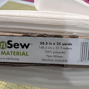 May include: A roll of white non-woven interfacing fabric. The label reads "58.5 in x 25 yards" and "100% polyester". The brand name "Pellon n Sew" is visible. The fabric is machine washable.