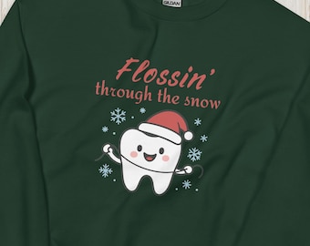 May include: A dark green sweatshirt with the phrase "Flossin' through the snow" in pink script. A cartoon tooth wearing a Santa hat is flossing. Snowflakes surround the tooth. Christmas decorations are in the background.