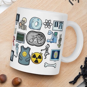 May include: White ceramic mug decorated with medical imagery, such as a skeleton, CT scan, and radiation symbol. The mug has a curved handle and is placed on a wooden board with nuts and decorative items.